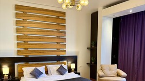 A modern bedroom with a large bed, wooden headboard, a chandelier, a leather armchair, and a desk with a chair. - Hildon Hotel Beirut (Beirut)