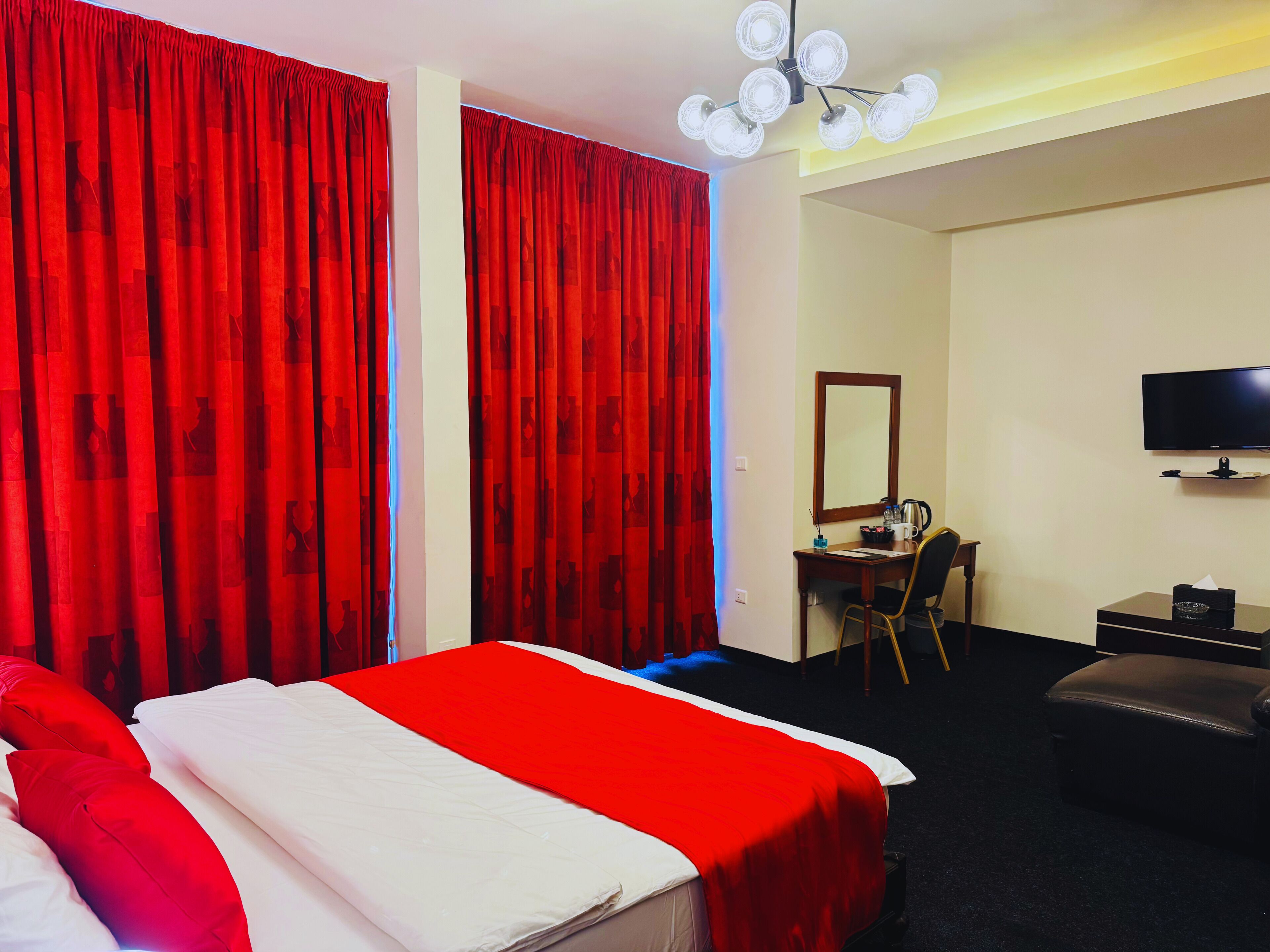 Habitación de hotel con una cama, un escritorio, una silla, un televisor y una cortina roja.