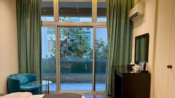 A modern hotel room with a large bed, a small round table, a blue chair, a large window with curtains, and a ceiling light. - Hildon Hotel Beirut (Beirut)