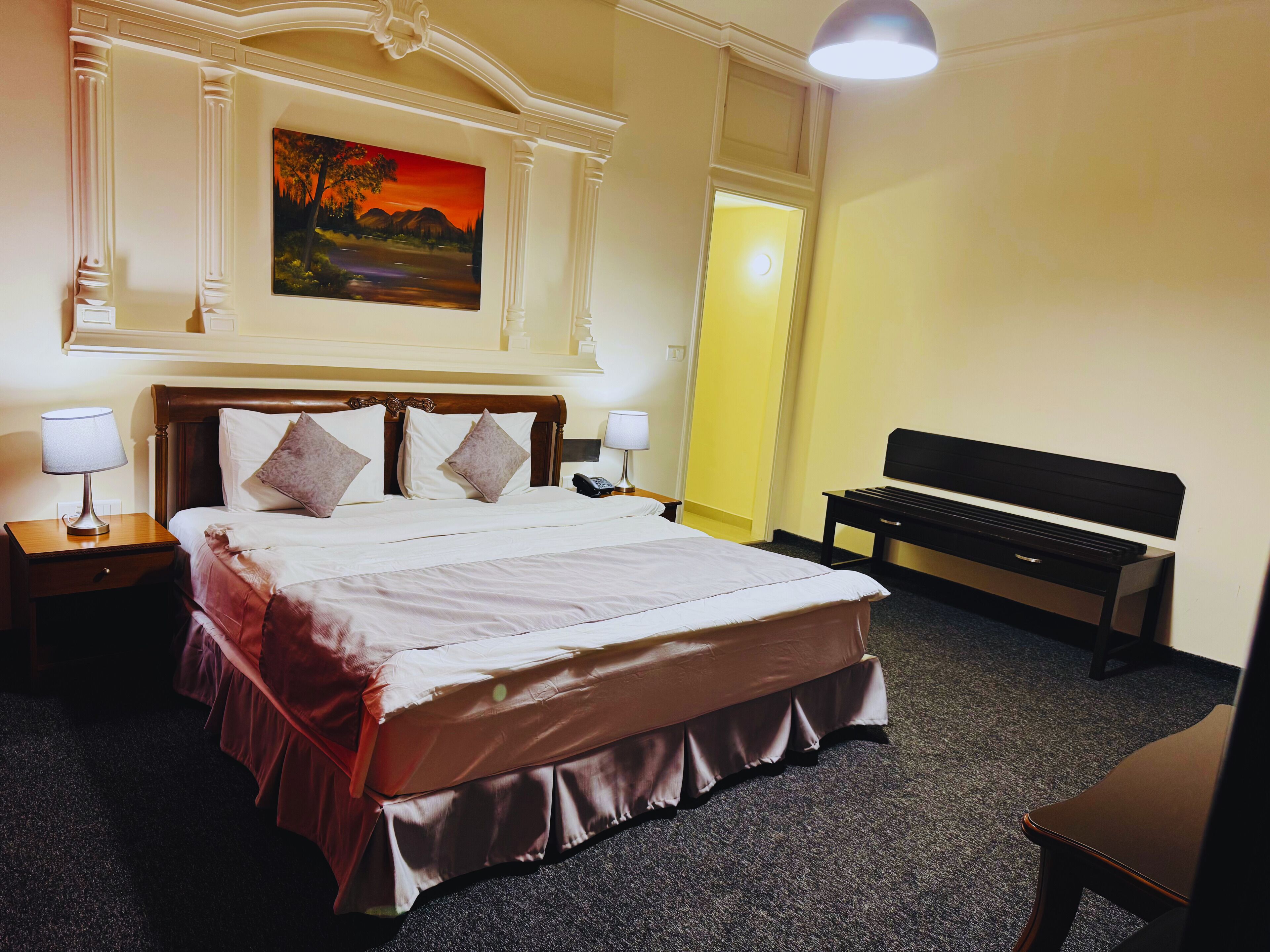 A hotel room with a large bed, two bedside tables, a bench, and a painting on the wall.