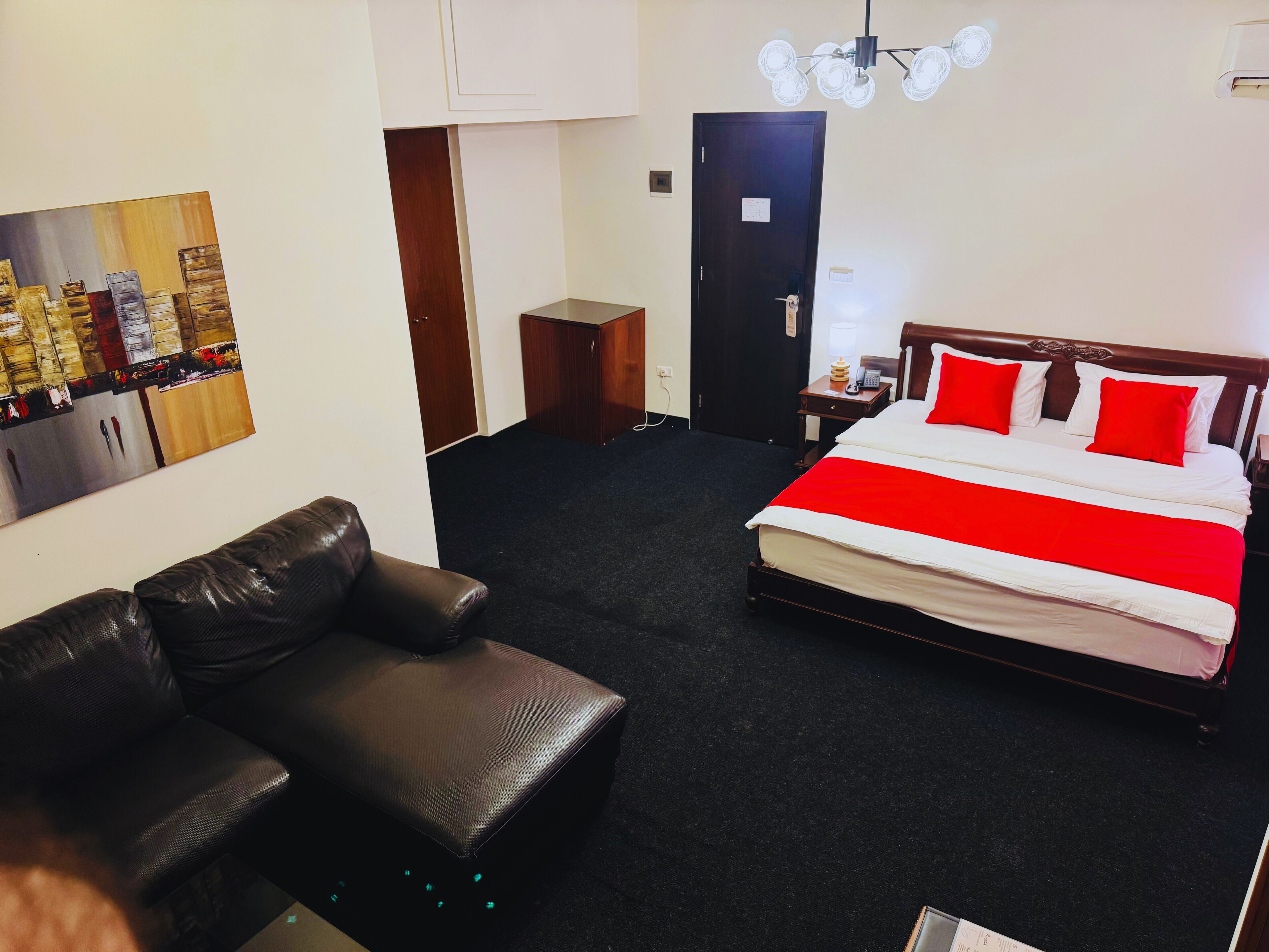 A hotel room with a bed, a leather sofa, a painting on the wall, and a door.