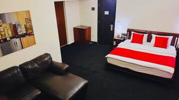 A hotel room with a bed, a leather sofa, a painting on the wall, and a door.