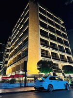 Eine mehrstöckige Parkgarage neben einem Hotel mit gelber Fassade, vor dem ein weißes Auto geparkt ist.