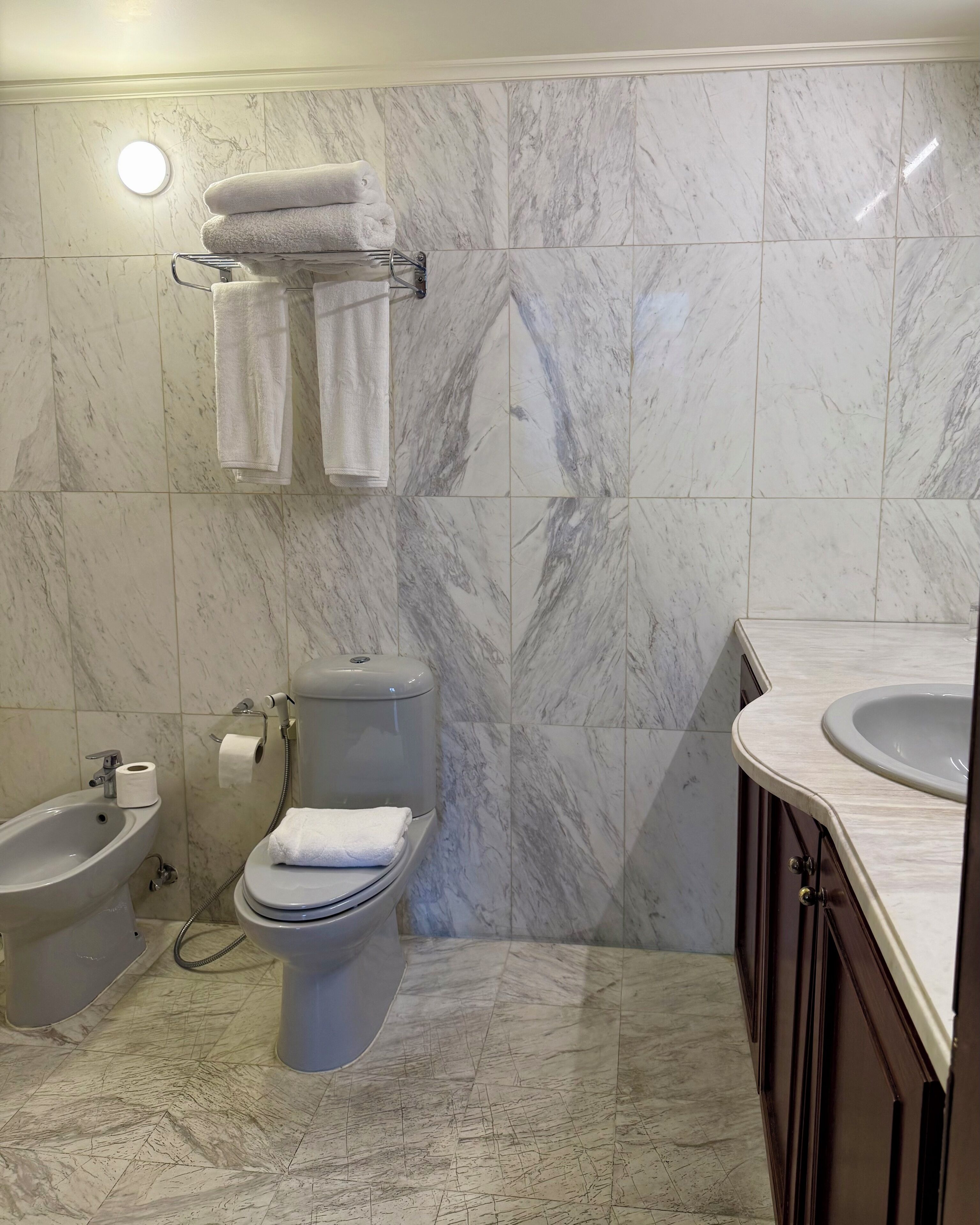 Un baño con bidé, inodoro, azulejos de mármol y lavamanos.