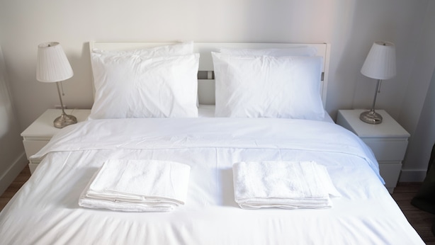 A neatly made bed with white linens and two folded towels on the bed. There are two bedside tables with lamps on either side of the bed. - Cozy flat in Kadıköy 2BR New House (İstanbul)