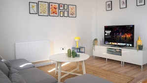 A modern living room with a flat-screen TV, grey sofa, white coffee table, and framed floral artwork on the wall. - Cozy flat in Kadıköy 2BR New House (İstanbul)