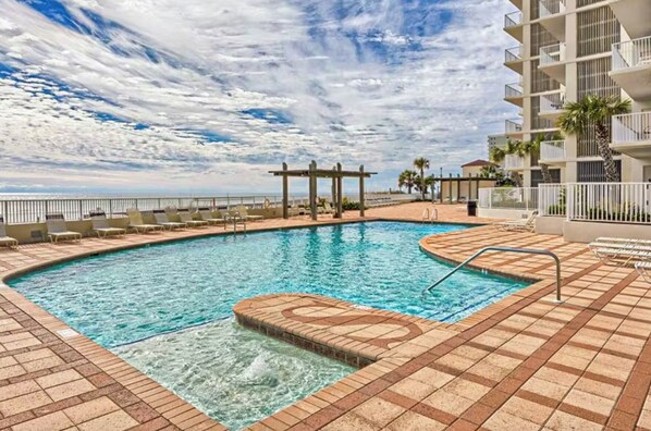 A pool area with a pergola, lounge chairs, and a view of the ocean.