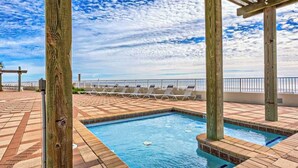 Piscina no terraço com vista para o oceano, rodeada por espreguiçadeiras e pilares de madeira.
