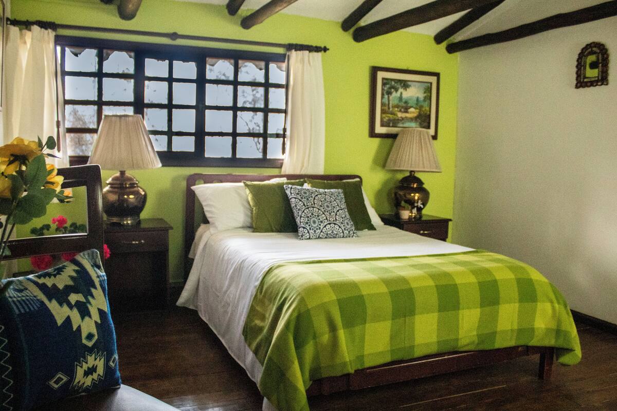Une chambre à coucher avec un lit, des rideaux verts, une fenêtre et un tableau accroché au mur.
