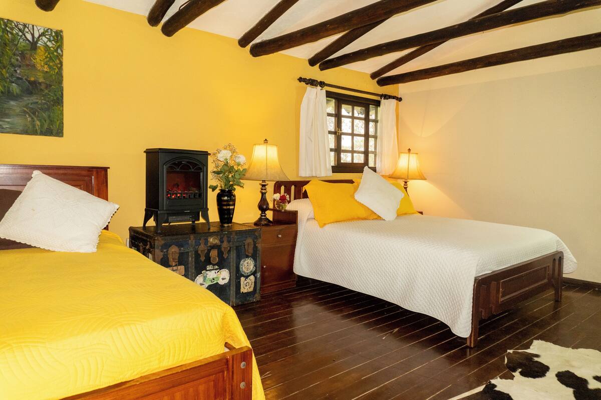 Une chambre avec deux lits, des poutres en bois au plafond, une fenêtre avec des rideaux et une table de chevet en bois avec une lampe.