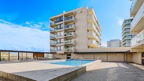 Un bâtiment moderne doté de nombreux balcons et d’un espace piscine sur le toit.