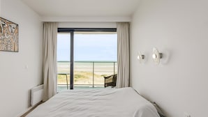 Une chambre avec un grand lit, une vue sur la plage et un fauteuil près de la fenêtre.