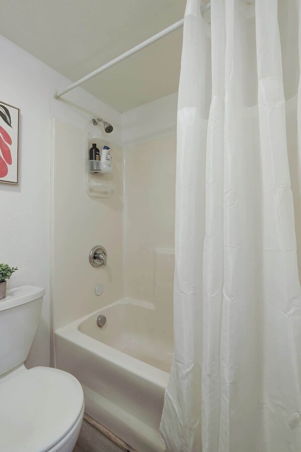 A bathroom with a bathtub, toilet, and shower curtain.