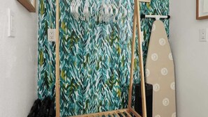 Ein Zimmer mit einem Wäscheständer aus Holz, einem Surfbrett und einer Wand mit Blättermuster.