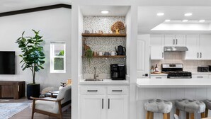 A modern kitchen with white cabinets, a central island with stools, and a dining area with a wooden table and chairs. - 3-bedroom Fireplace Stunning Spanish Home (Indio)