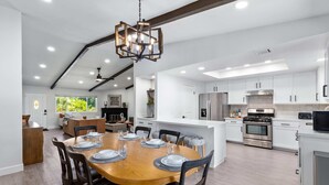 A modern kitchen with white cabinets, stainless steel appliances, and a wooden dining table set for six. - 3-bedroom Fireplace Stunning Spanish Home (Indio)