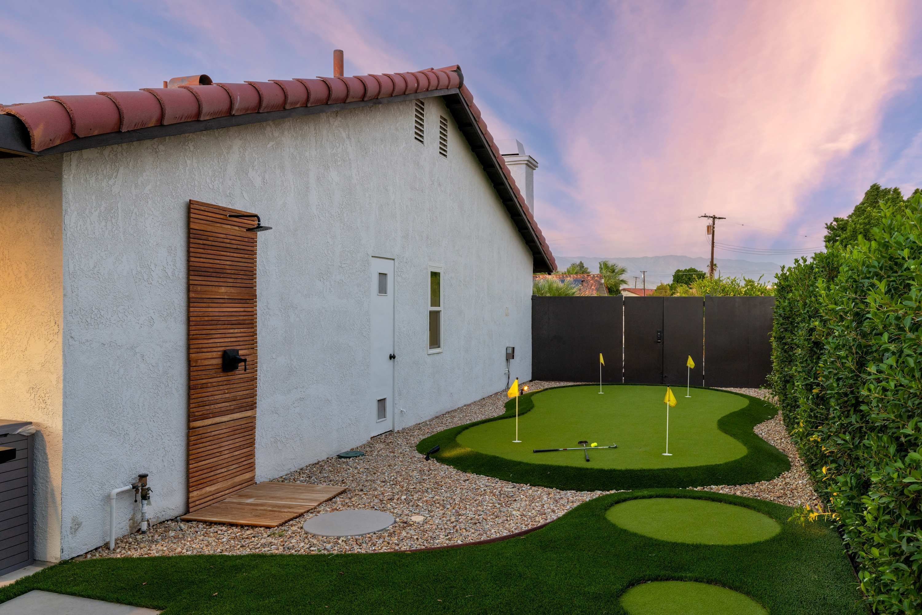 Una casa con facciata bianca, una porta in legno e un piccolo giardino anteriore con erba sintetica e un putting green.