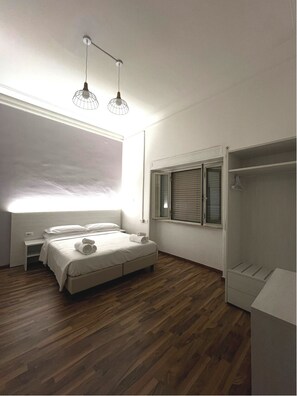A modern bedroom with a large bed, two pendant lights, a window with blinds, and a walk-in closet. - Green Park San Pancrazio (Rome)