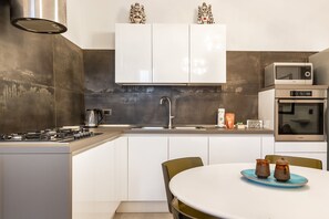 Una cucina moderna con mobili bianchi, una cappa aspirante in acciaio inossidabile, un forno a microonde e un forno.