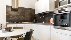 A modern kitchen with white cabinets, a stainless steel range hood, a built-in oven, and a round dining table with chairs. - Nicu Amuri con Terrazza a Noto by Wonderful Italy (Noto)