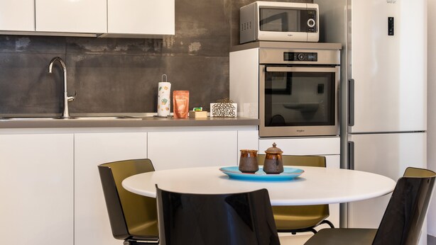 A modern kitchen with a microwave, oven, and refrigerator. There is a sink with a faucet, a table with chairs, and a blue tray with two jars. - Nicu Amuri con Terrazza a Noto by Wonderful Italy (Noto)