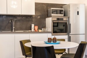 A modern kitchen with a microwave, oven, and refrigerator. There is a sink with a faucet, a table with chairs, and a blue tray with two jars. - Nicu Amuri con Terrazza a Noto by Wonderful Italy (Noto)