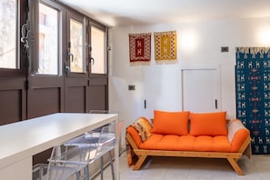 A room with a wooden sofa, a white table, and a window with curtains. - Nicu Amuri con Terrazza a Noto by Wonderful Italy (Noto)