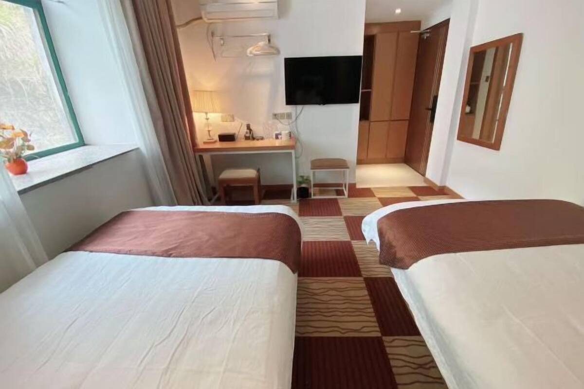 A hotel room with two beds, a desk, a TV, and a window with curtains.