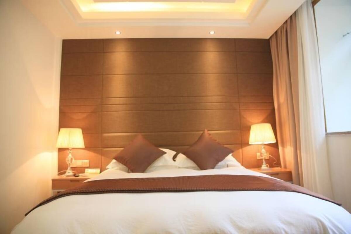 A hotel room with a large bed, two bedside lamps, a headboard, and a window with curtains.