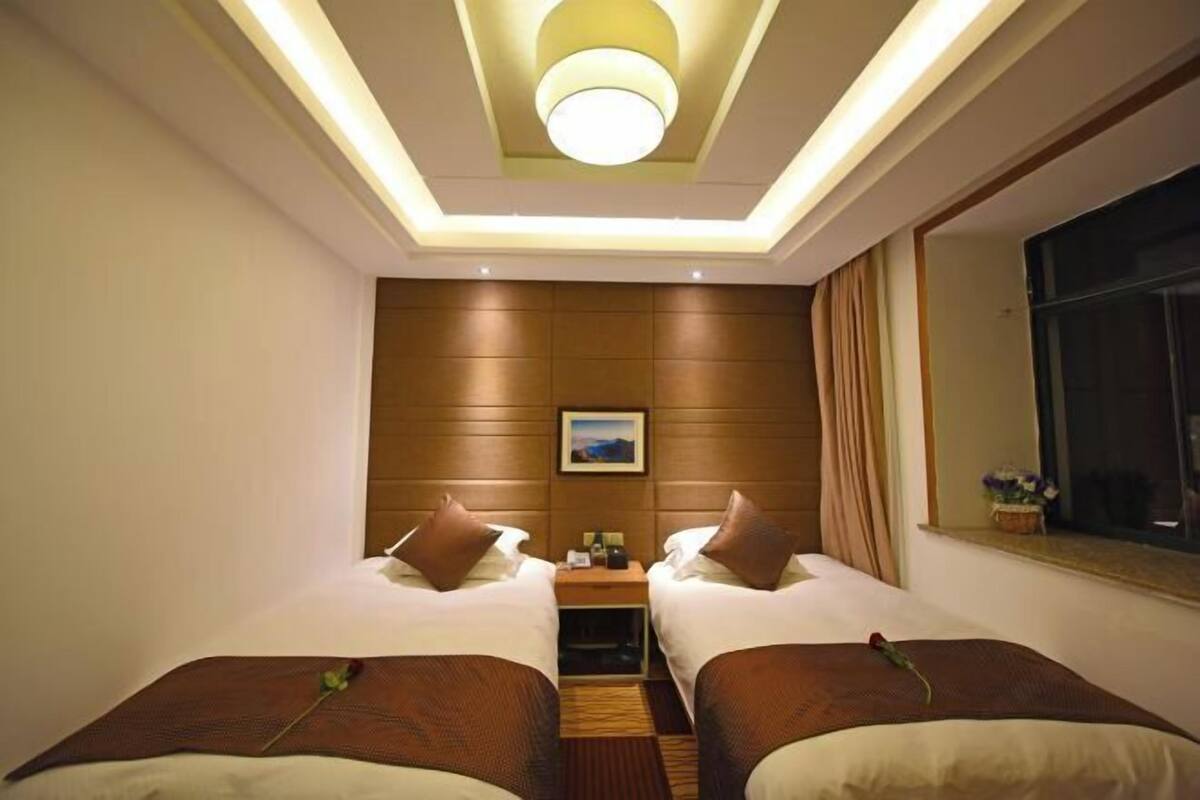A hotel room with two beds, a nightstand, a window with curtains, and a ceiling light fixture.