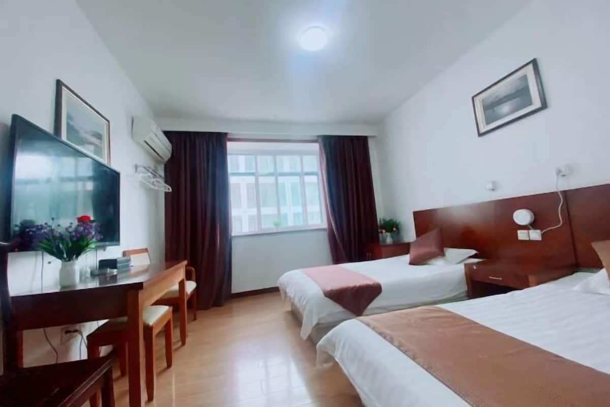 A hotel room with two beds, a desk with a chair, a television, and a window with curtains.