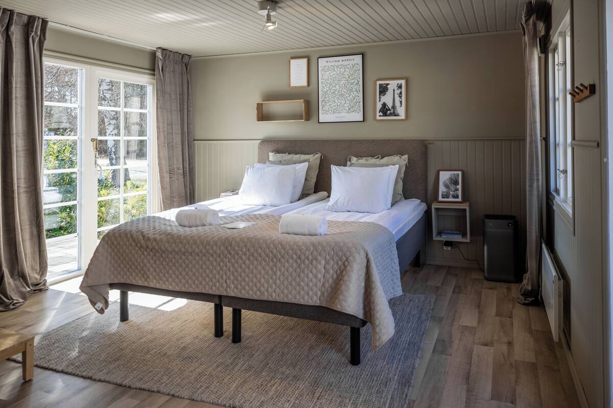 A bedroom with a large bed, a bedside table, a radiator, and a view of the outdoors.
