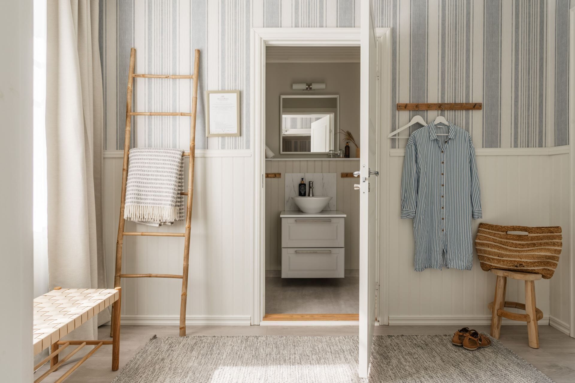 Un baño con una escalera de madera, un lavabo, un espejo y una percha con ropa.