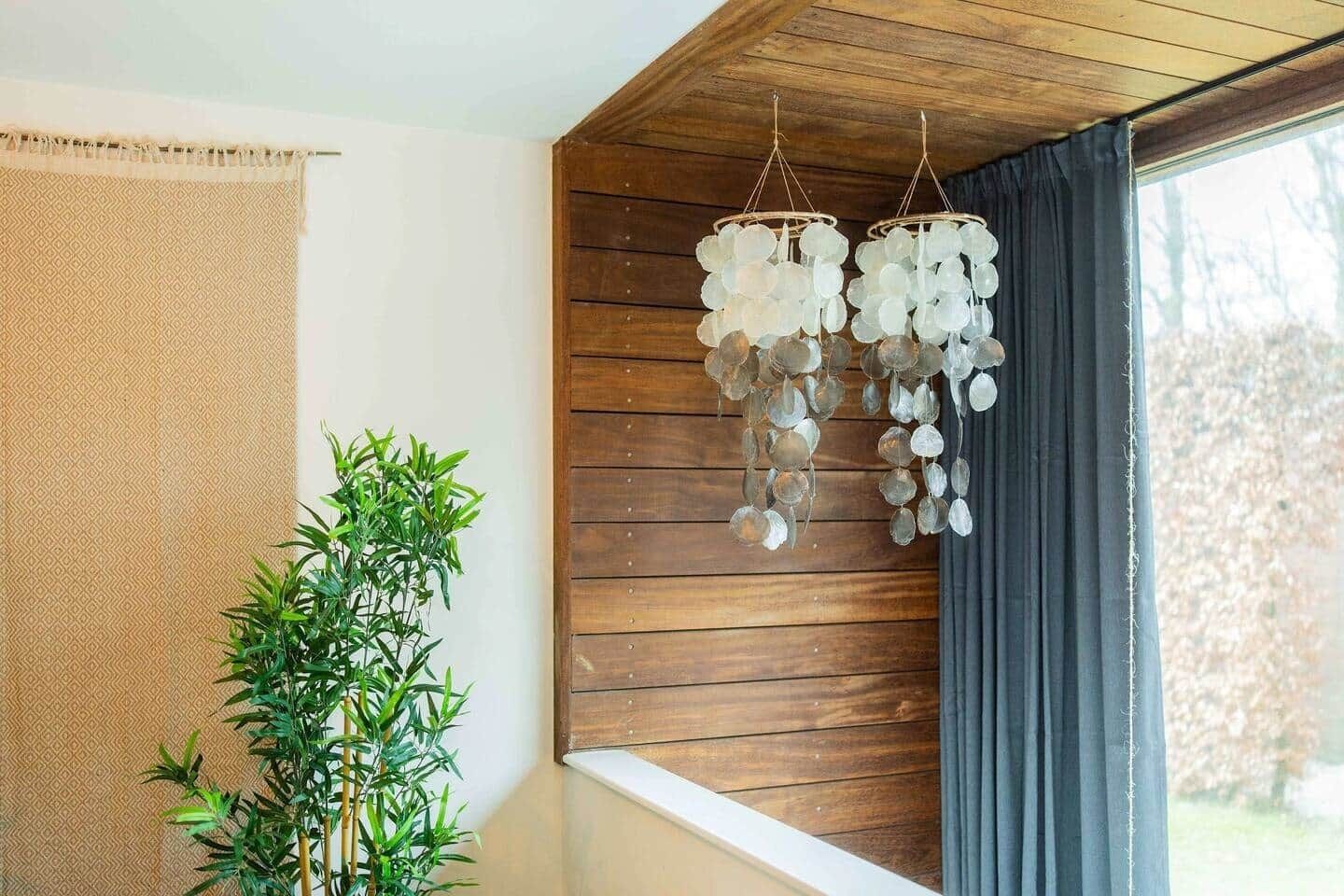 Une pièce avec un plafond en bois, une fenêtre avec des rideaux, un luminaire suspendu et une plante en bambou.