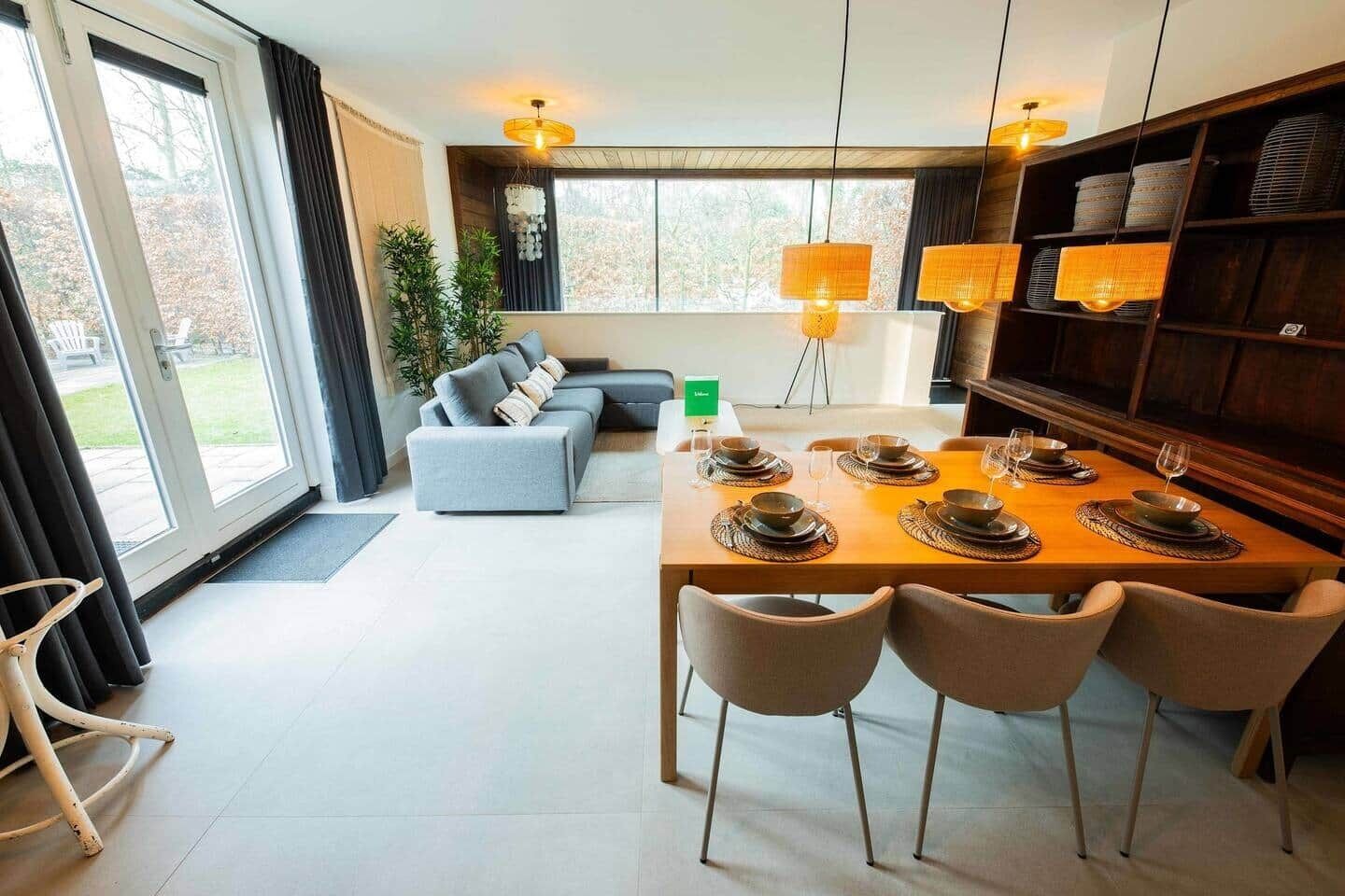 Een moderne woonkamer met een eethoek, grote ramen en een bank.