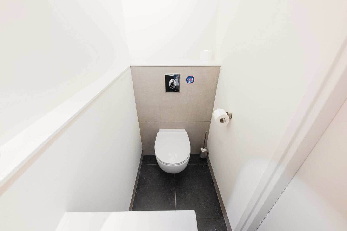 A small, narrow bathroom with a white toilet, a hand dryer, and a toilet paper holder.