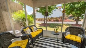 Un patio techado con mobiliario de mimbre y cojines amarillos, suelo a cuadros y vistas a una zona residencial.