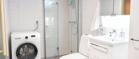 Een moderne badkamer met een Bosch wasmachine, een douche met glazen wanden en een witte wastafel met spiegel.