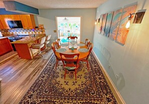 Enjoy meals in this stylish dining area with a wooden table and comfortable chairs, surrounded by vibrant artwork and modern appliances.