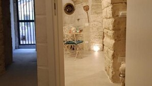 A narrow hallway with a rustic stone wall and a white door on the left. A small table with a chair is visible in the distance, and a decorative item hangs on the wall. - Dimora D'Archi in the beating heart of Bari's Borgo Antico  (Bari)