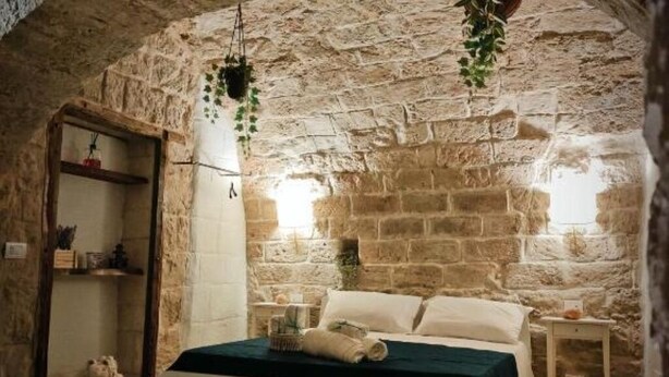 A rustic stone-walled bedroom with a bed, a small table, and a hanging plant. - Dimora D'Archi in the beating heart of Bari's Borgo Antico  (Bari)