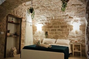 Camera da letto rustica con pareti in pietra, un letto, un tavolino e una pianta pensile.