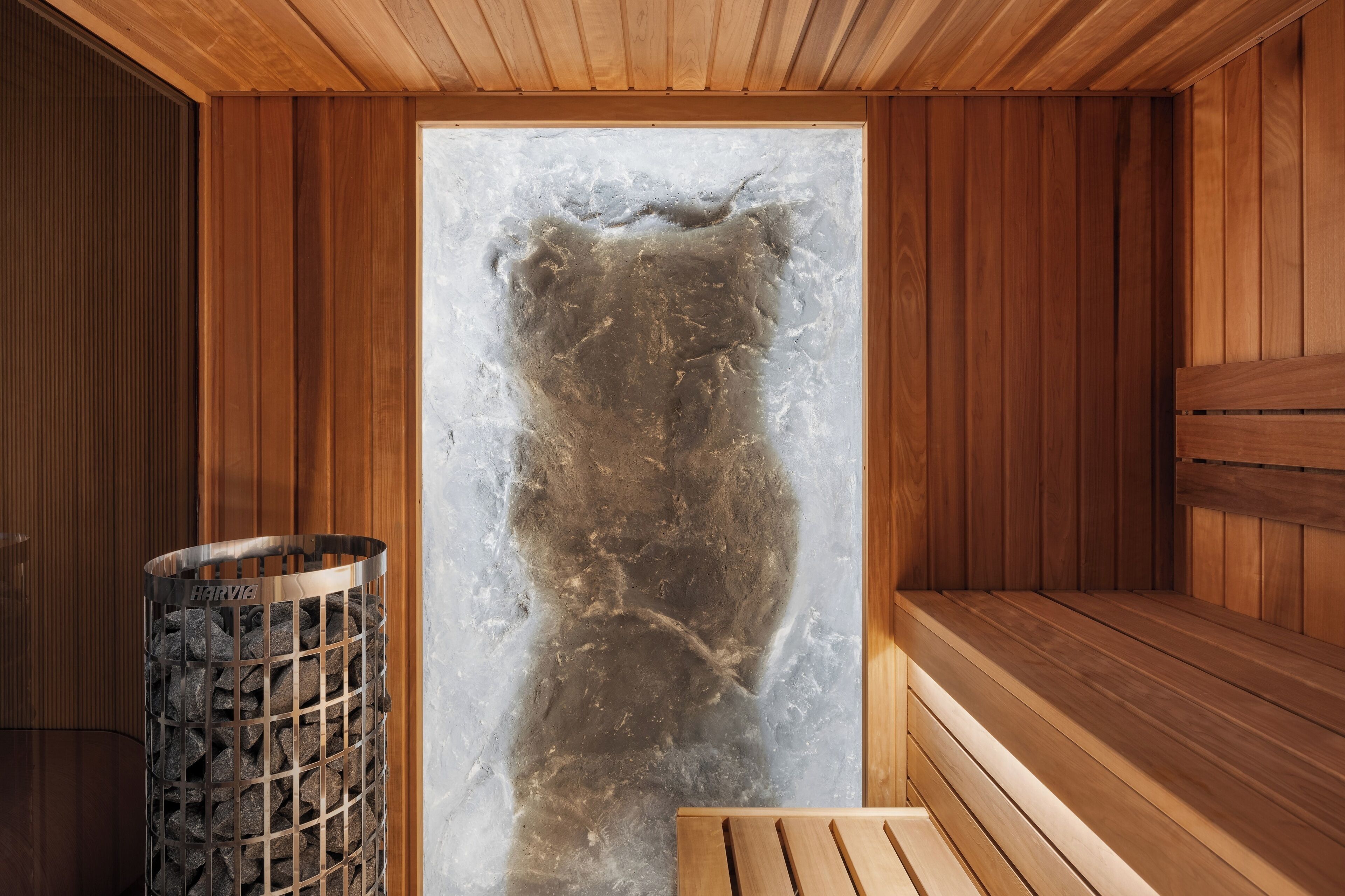 A sauna room with wooden walls, a bench, and a stone wall with a metal grate.
