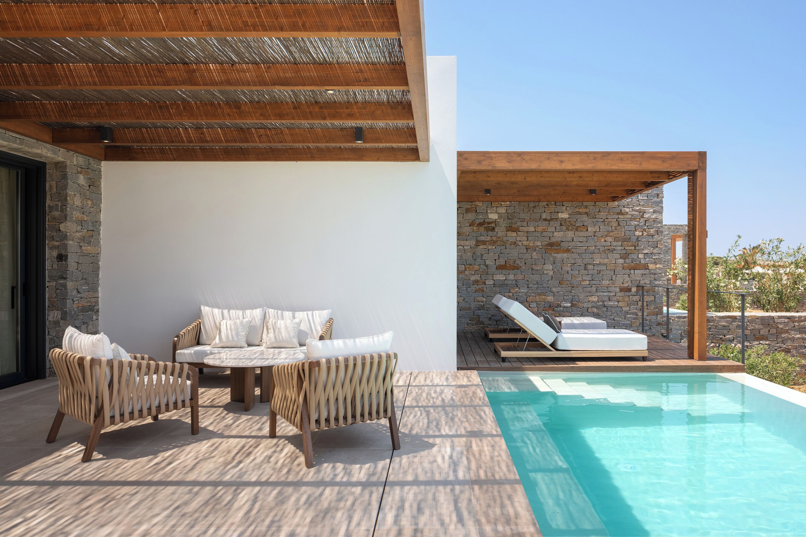 A modern outdoor pool area with a stone wall, wooden deck, and lounge chairs.