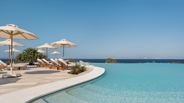 Un área junto a la piscina con sillones de descanso y sombrillas, una piscina azul cristalina y vistas al océano.