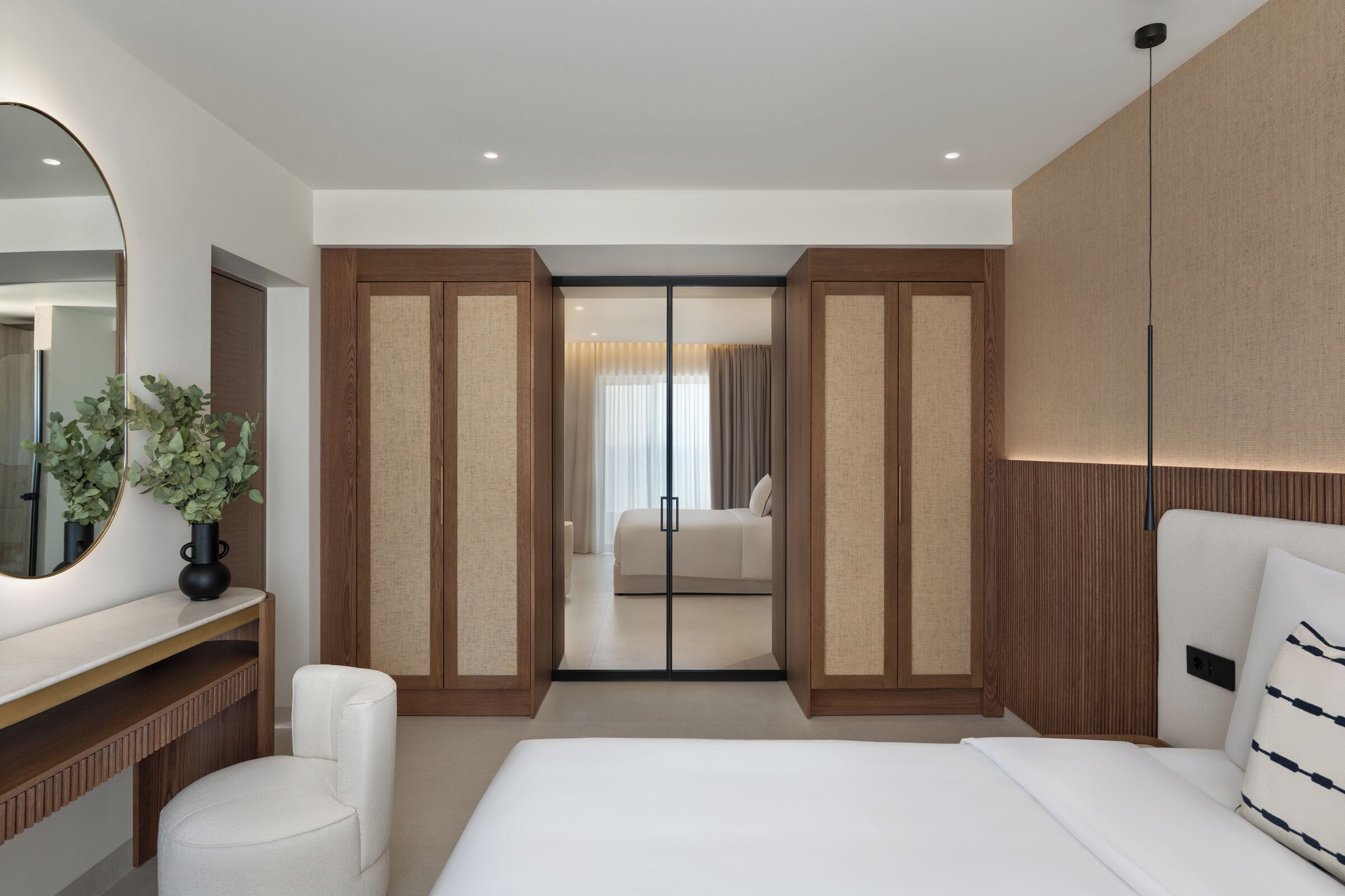A modern bedroom with a large bed, a bedside table with a mirror, a chair, and a wardrobe with a sliding door.