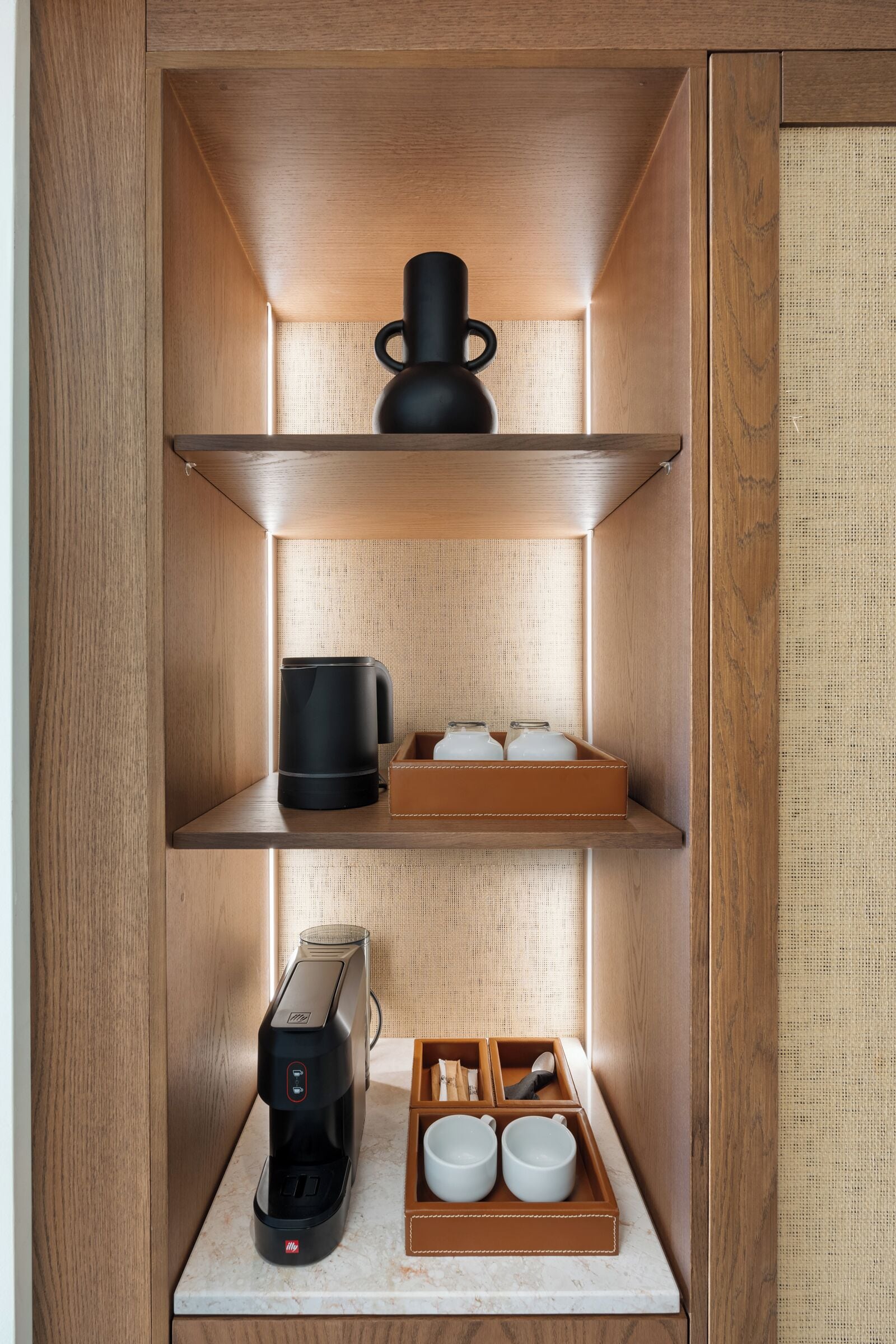 A compact kitchen with a coffee maker, a kettle, and a tray with cups and utensils.