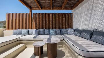 A modern outdoor seating area with a curved sofa, two round wooden tables, and a wooden pergola overhead.