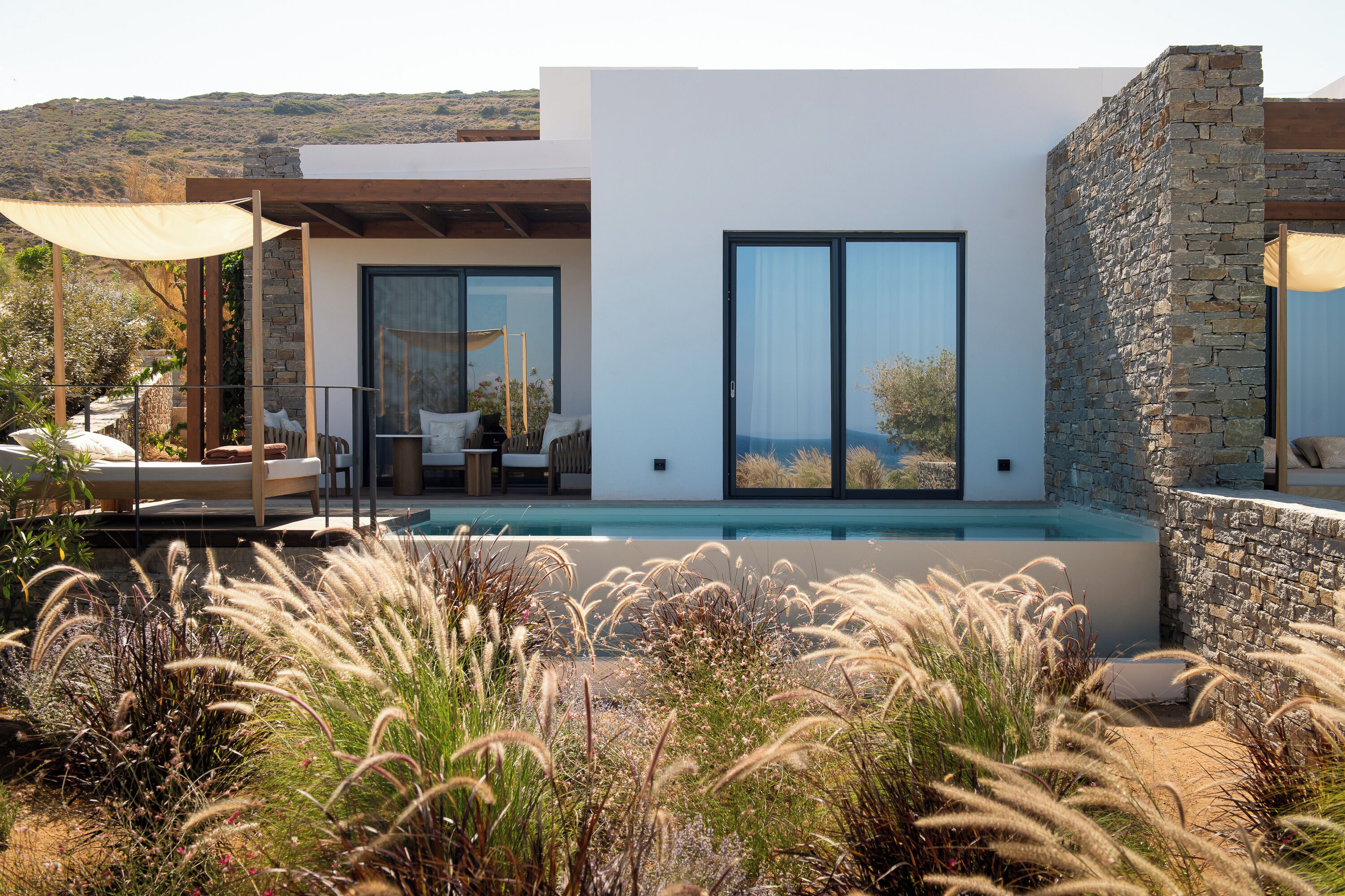 A modern house with a pool, outdoor seating, and a stone wall.