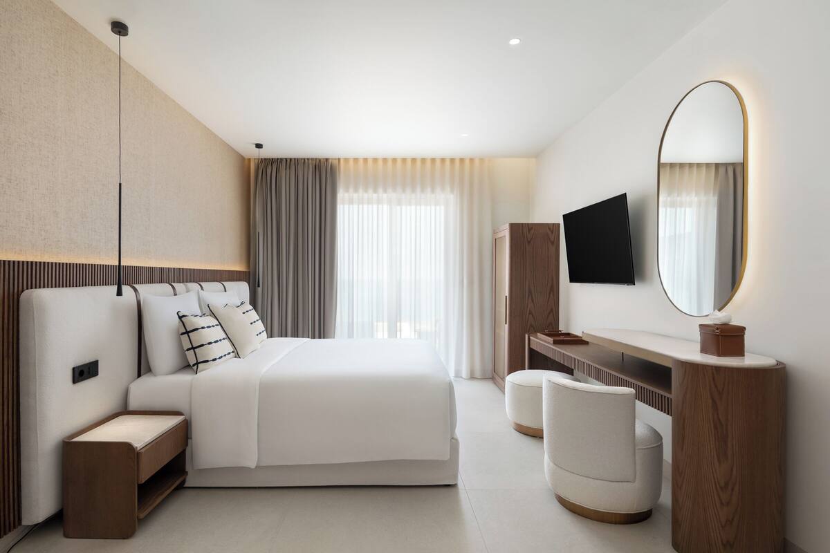 A modern hotel room with a large bed, a vanity with a mirror, and a television mounted on the wall.